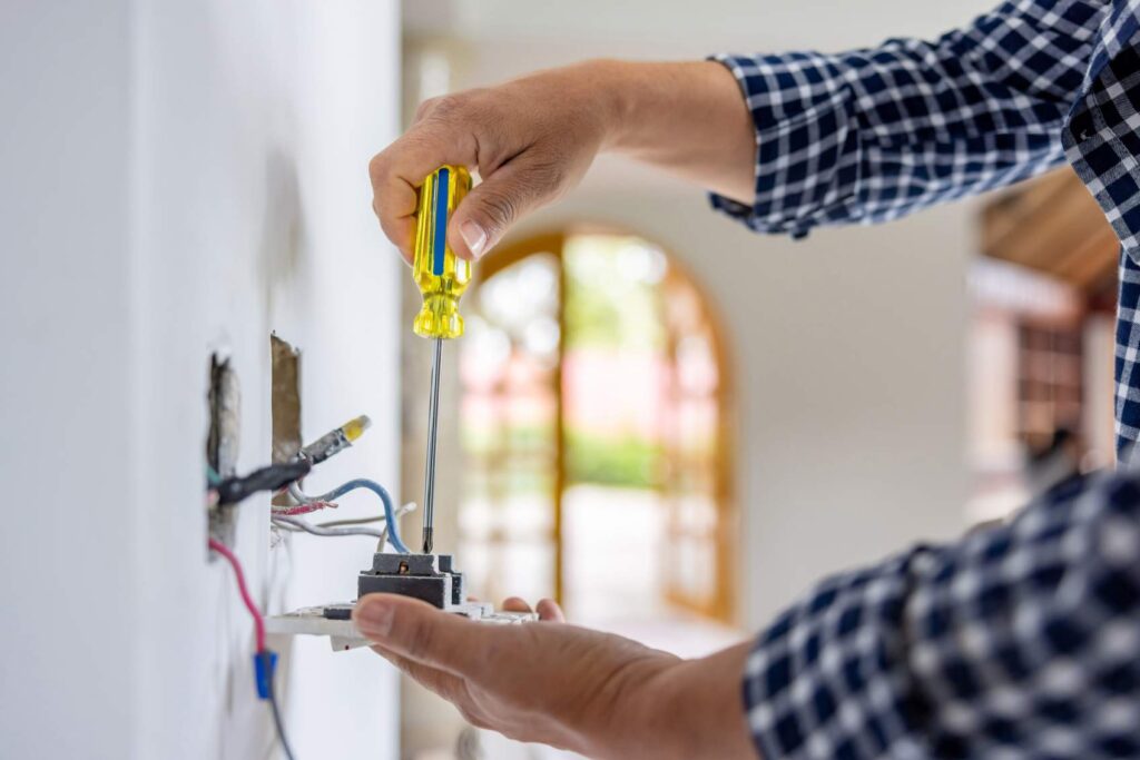 Electrician installing power outlet indoors to protect against surges in Dedham, MA