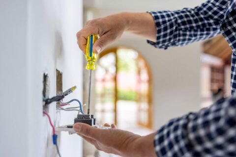 Electrician installing power outlet indoors to protect against surges in Dedham, MA