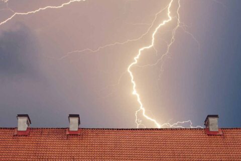 Nighttime thunderstorm with lightning bolt over rooftop in Dedham, MA