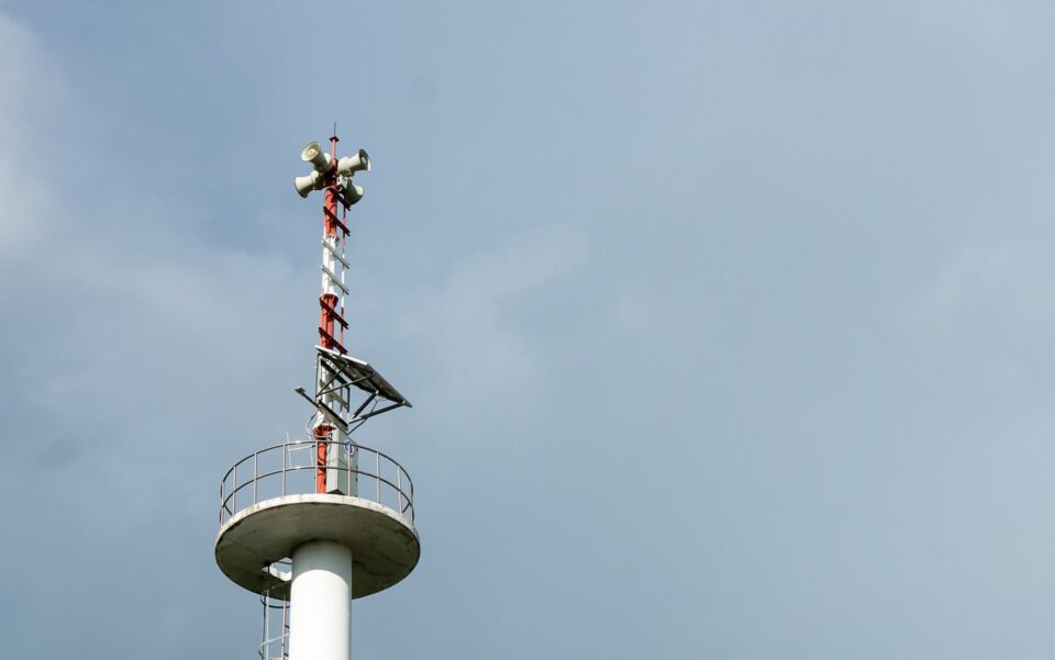 Tall warning tower with lightning rod and speakers against a cloudy sky in Dedham, MA